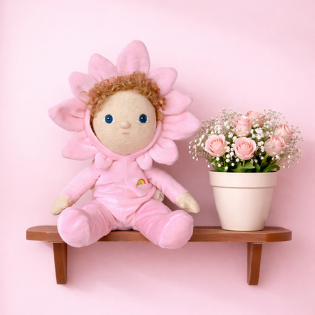 Olli Ella Dinky Dinkum Doll Magnolia in pink flower suit on a wooden shelf next to pink roses.