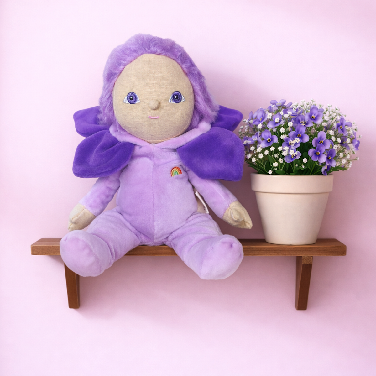 Dinky Dinkums Violet doll sitting on a wooden shelf next to a potted plant with purple flowers.