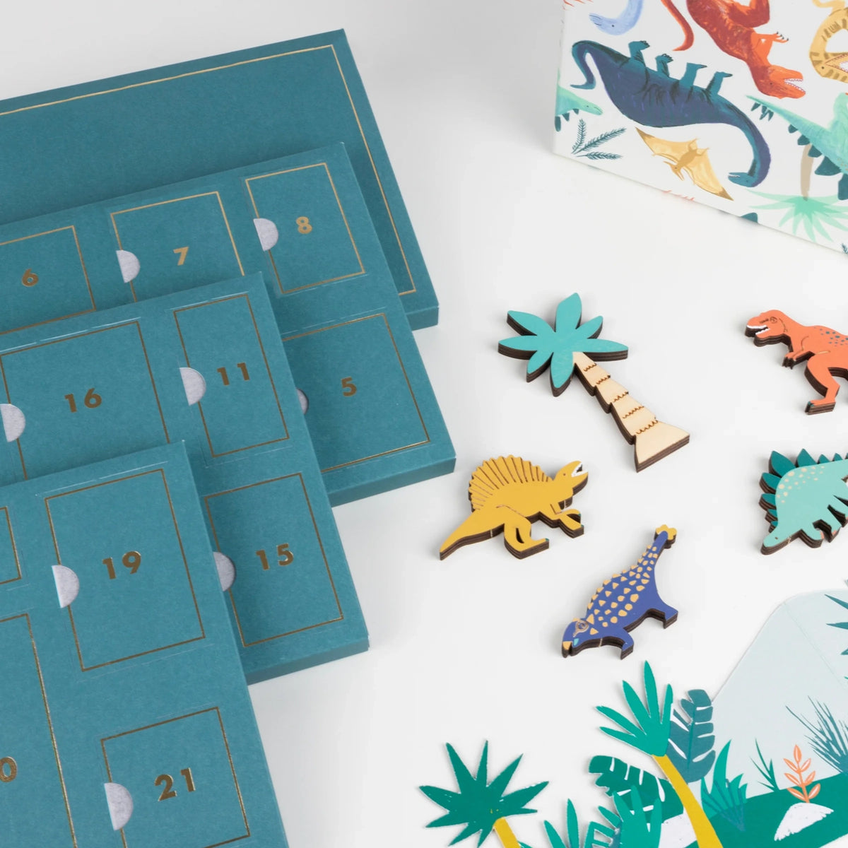 Numbered teal advent calendar trays displayed next to wooden dinosaur toys and paper decorations.