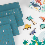 Numbered teal advent calendar trays displayed next to wooden dinosaur toys and paper decorations.