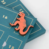 Small wooden T-Rex figure resting on a numbered teal advent calendar tray.