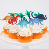 Cupcakes with swirled white frosting, dinosaur and palm tree toppers, and metallic orange baking cups on a white plate.