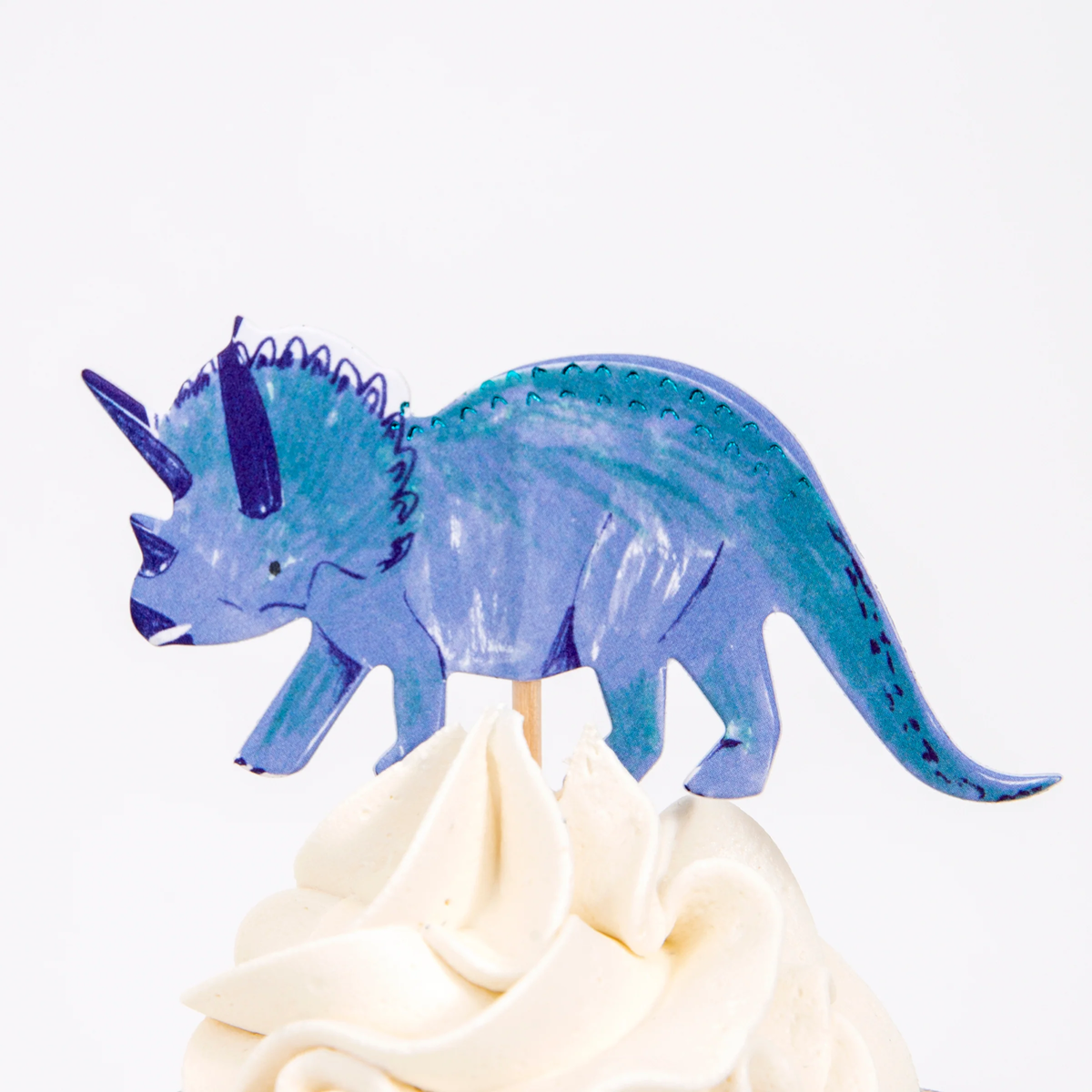 Blue triceratops cupcake topper on a wooden pick in swirled white frosting.