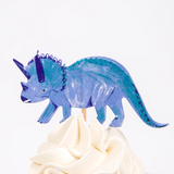 Blue triceratops cupcake topper on a wooden pick in swirled white frosting.