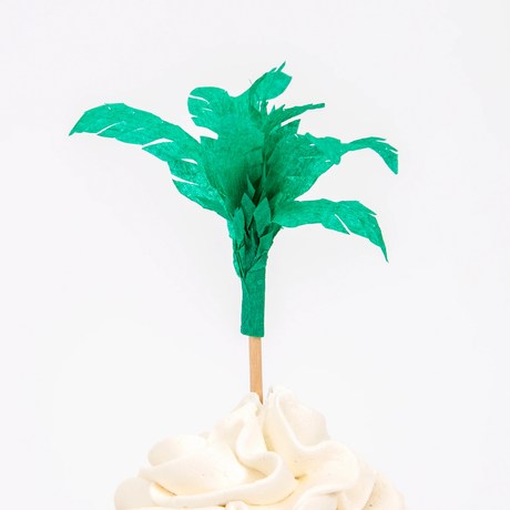 Green tissue paper palm tree cupcake topper on a wooden pick in swirled white frosting.