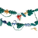 Close-up of a dinosaur garland with tropical leaves and colorful dinosaur cutouts against white.