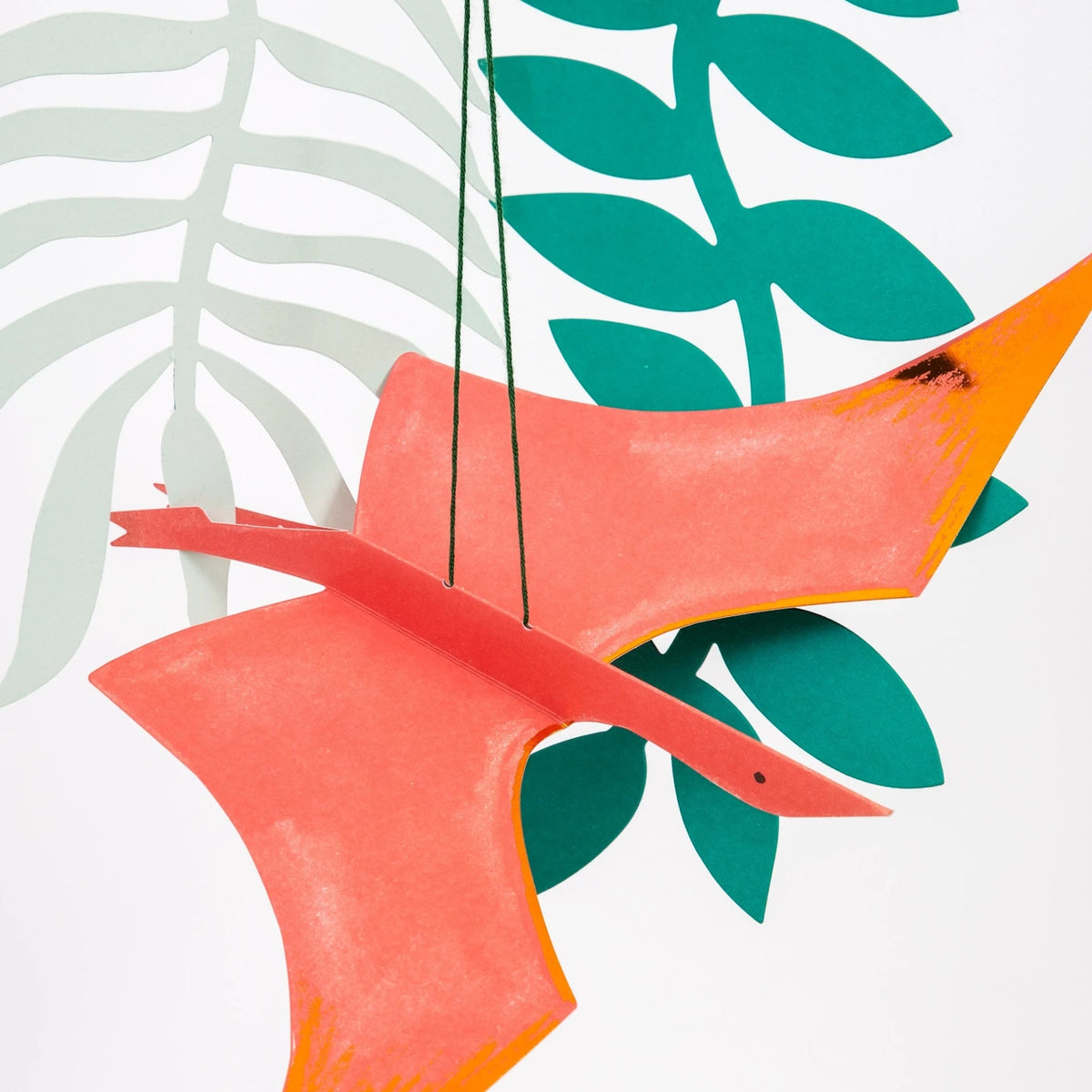 Close-up of a 3D red and orange flying pterodactyl paper cutout suspended from green cord against a background of paper leaves.