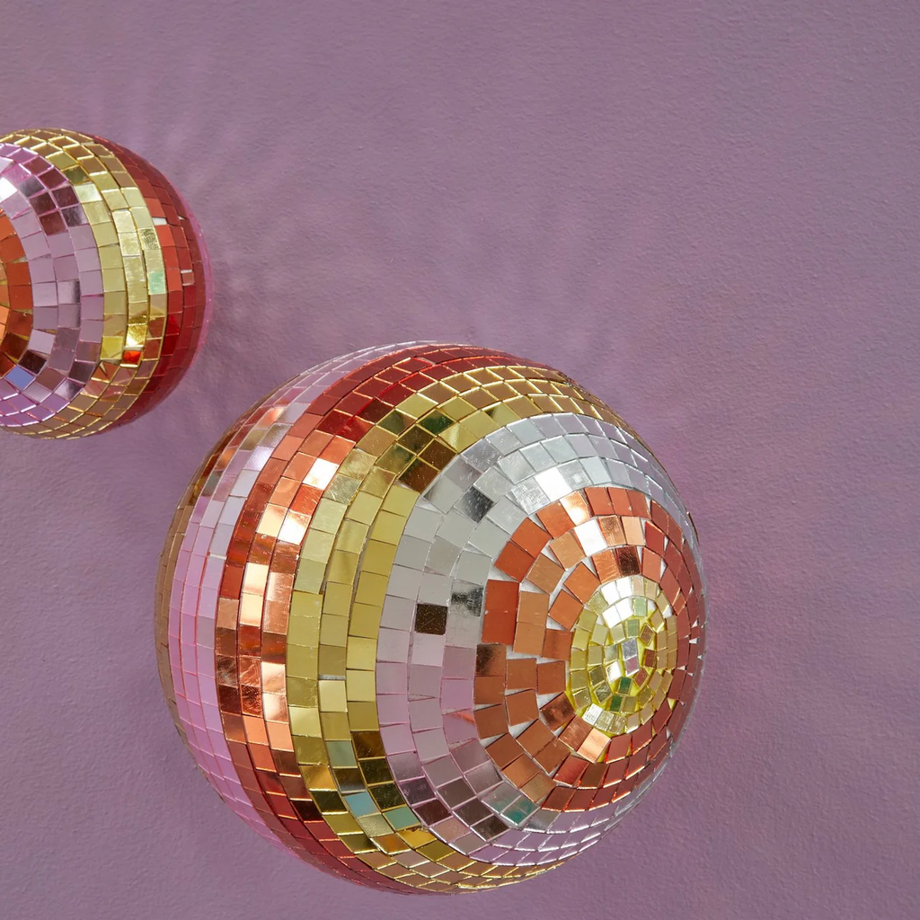Mosaic spheres with colorful tiles in red, pink, yellow, and silver tones reflect light against a soft purple wall, creating a festive ambiance.