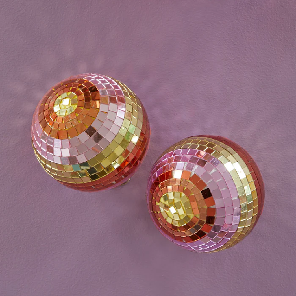 Two colorful disco balls with pink, gold, and orange mosaic tiles are placed on a purple surface, casting a playful and vibrant mood.