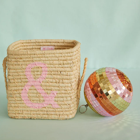 A woven straw basket with a pink ampersand next to a pink, gold, and green striped disco ball.