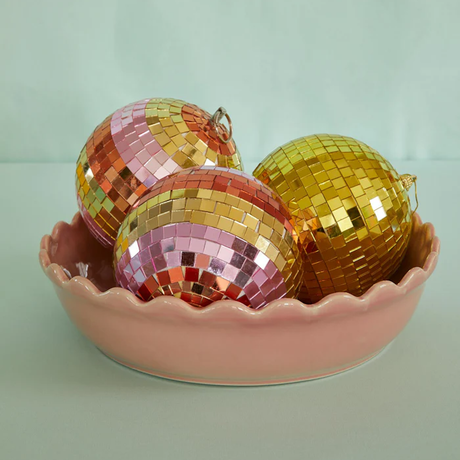Three colorful and gold mosaic disco balls sitting inside a pink scalloped ceramic bowl.