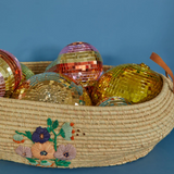 Colorful striped and gold disco balls resting inside an embroidered woven straw basket against a blue wall.
