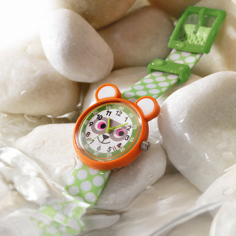 Raccoon-themed children's watch with a green polka-dot strap resting on smooth white stones in water.