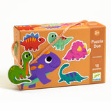 Orange puzzle box with colorful cartoon dinosaurs, featuring a handle. Text reads “Puzzle Duo,” “10 puzzles,” and “2+” in playful fonts.