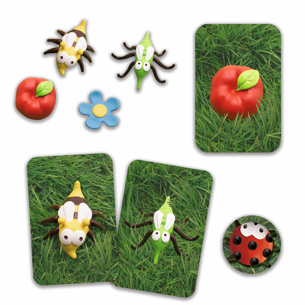 A whimsical collection of clay figures includes a bee, fly, red apple, blue flower, ladybug, and cards featuring these items on grass. Playful tone.
