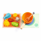 A colorful children's play dining set with two plates, cups, utensils, and toy food, accompanied by two cartoon cats.