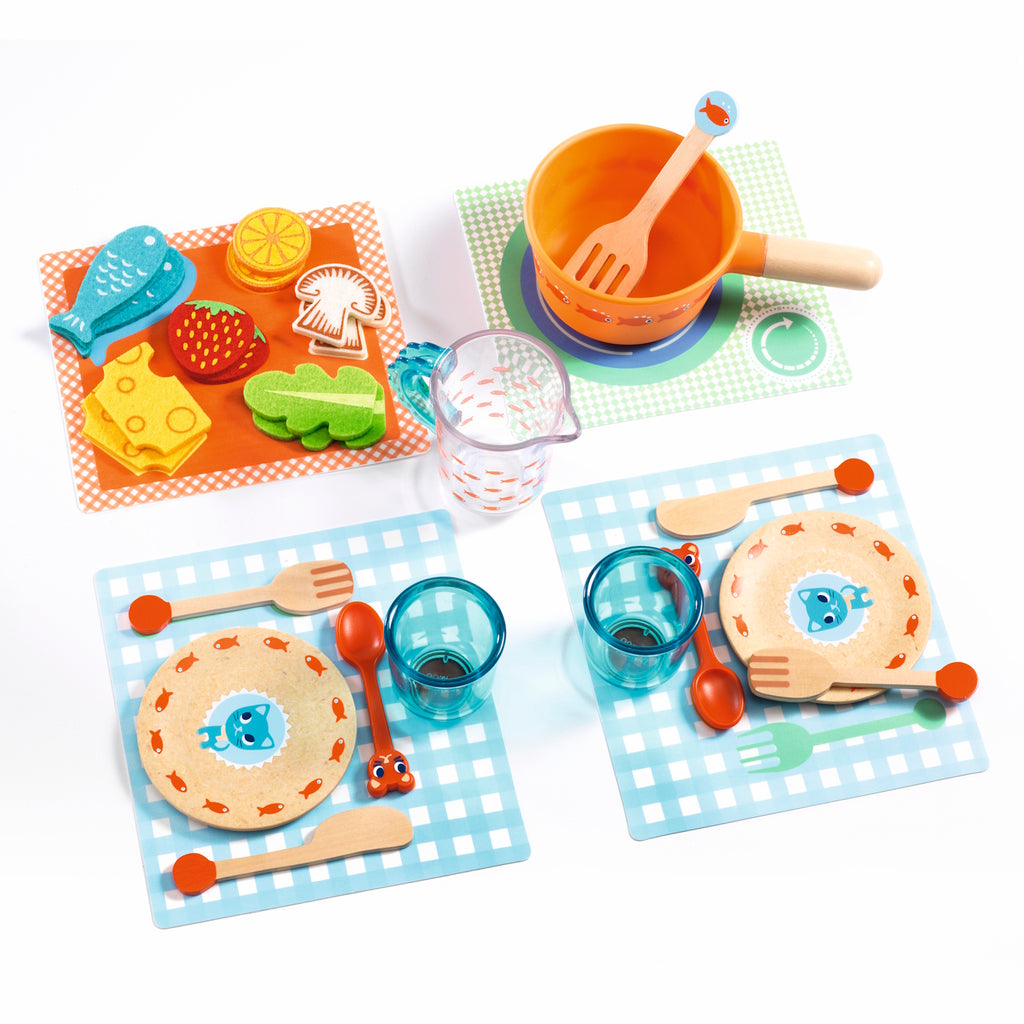 A colorful children's play dining set with two plates, cups, utensils, and toy food, accompanied by two cartoon cats.