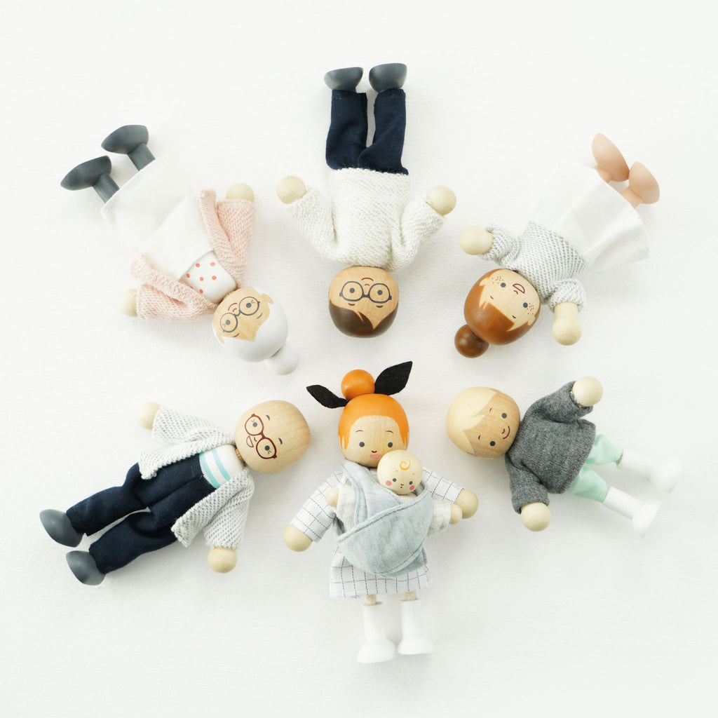 A cheerful wooden doll family with varied skin tones and outfits, including grandparents, parents, and children, all smiling joyfully together.