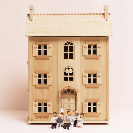 Seven wooden family figures and a dog toy standing in front of a three-story wooden dollhouse.