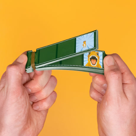 Hands flipping through a filmstrip-styled dinosaur animation flip book against a bright yellow background.