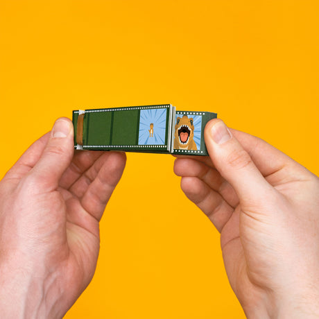 Hands holding a dinosaur flip book against a bright yellow background, showing two animation frames.