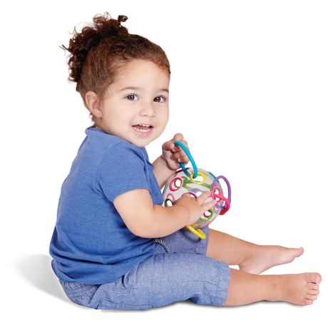 A smiling toddler in a blue outfit sits playfully on the floor, holding a colorful toy ball with loops. The mood is joyful and engaging.