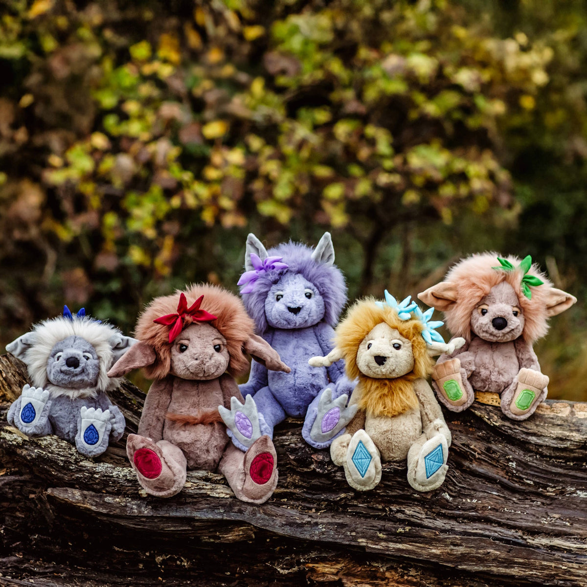 Five colorful plush troll toys lined up outdoors, sitting together on a fallen tree log.