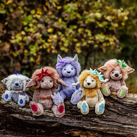 Five colorful plush troll toys lined up outdoors, sitting together on a fallen tree log.