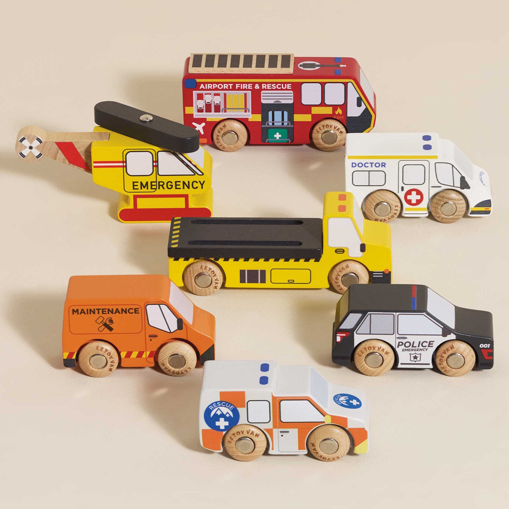Toy wooden vehicles, including a yellow emergency helicopter, fire truck, maintenance van, dump truck, police car, ambulance, and rescue vehicle, each with colorful details.