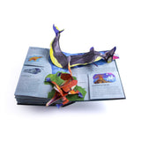 A colorful pop-up book page featuring a large sea monster and a smaller creature emerging in 3D paper art. Text and ocean imagery surround them, creating an adventurous tone.