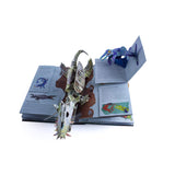 A pop-up book open to two pages with colorful 3D dinosaur figures emerging, including a striped dinosaur and a blue one, creating an interactive and playful scene.