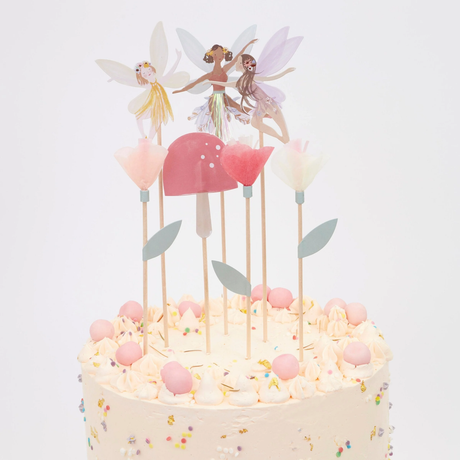 Frosted cake decorated with paper fairy toppers, tissue paper flowers, and a pink toadstool on wooden picks.