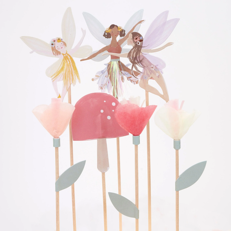 Paper fairy cake toppers with tissue paper flowers and a pink toadstool on wooden picks.