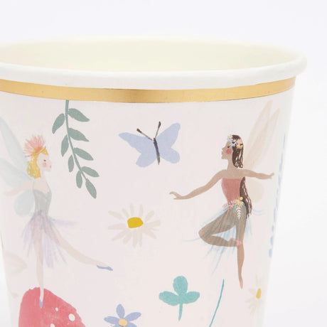 Paper cup with a gold rim, decorated with illustrations of dancing fairies and a blue butterfly.