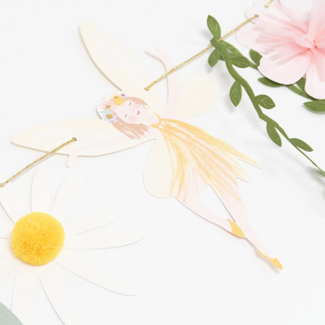 Close-up of a fairy garland cutout wearing a yellow dress next to a paper daisy with a pom-pom center.
