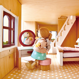 A wooden doll looks into a vanity mirror inside a miniature dollhouse bedroom.