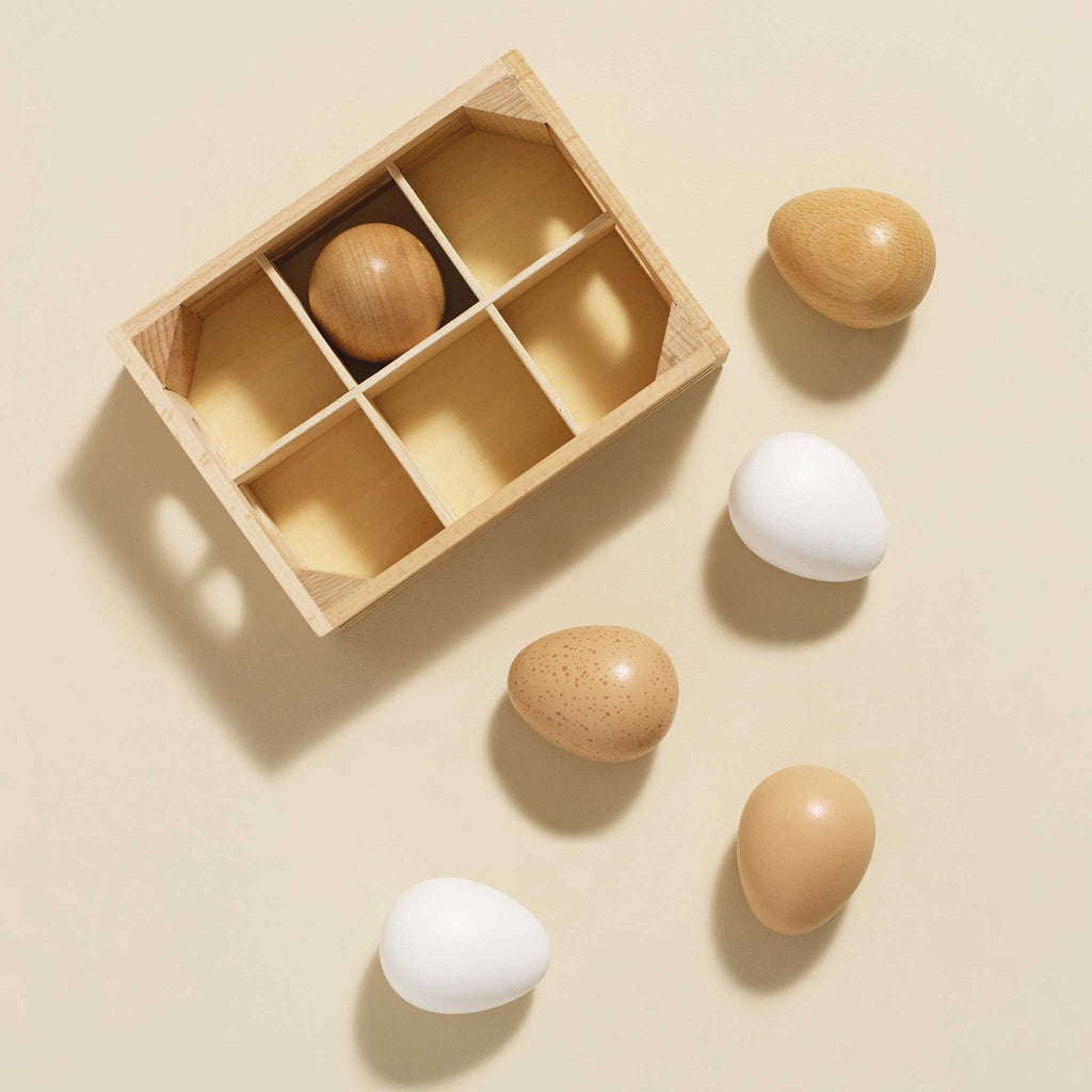 Wooden crate holding five toy eggs in white, tan, and speckled brown.