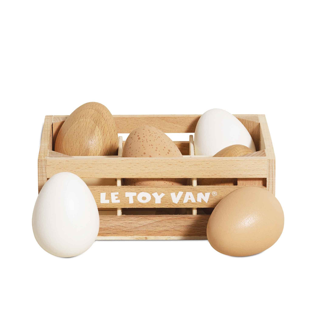 Wooden crate labeled "LE TOY VAN" holding five toy eggs in white, tan, and speckled brown. Two eggs are placed outside the crate, depicting a playful scene.