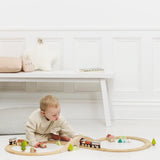 Young toddler playing with a wooden train set on the floor in a brightly lit room.