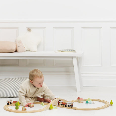 Young toddler playing with a wooden train set on the floor in a brightly lit room.