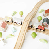 Wooden toy train set with tracks, overpass bridge, buildings, and trees.