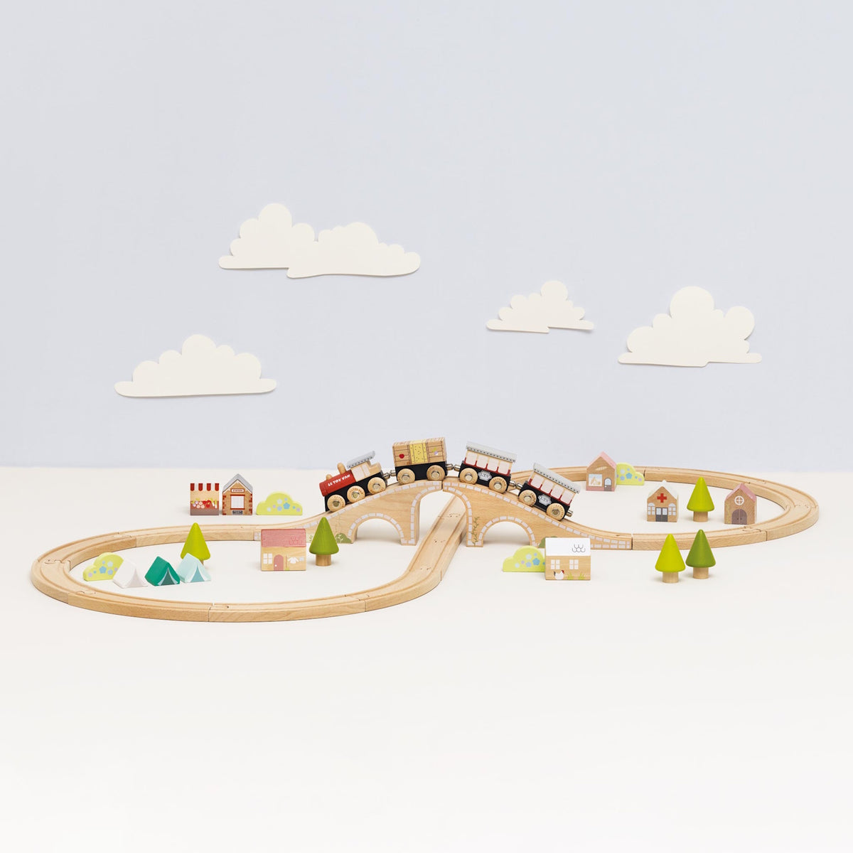 Wooden figure-8 toy train set with a train crossing over a bridge, surrounded by mini trees and houses.