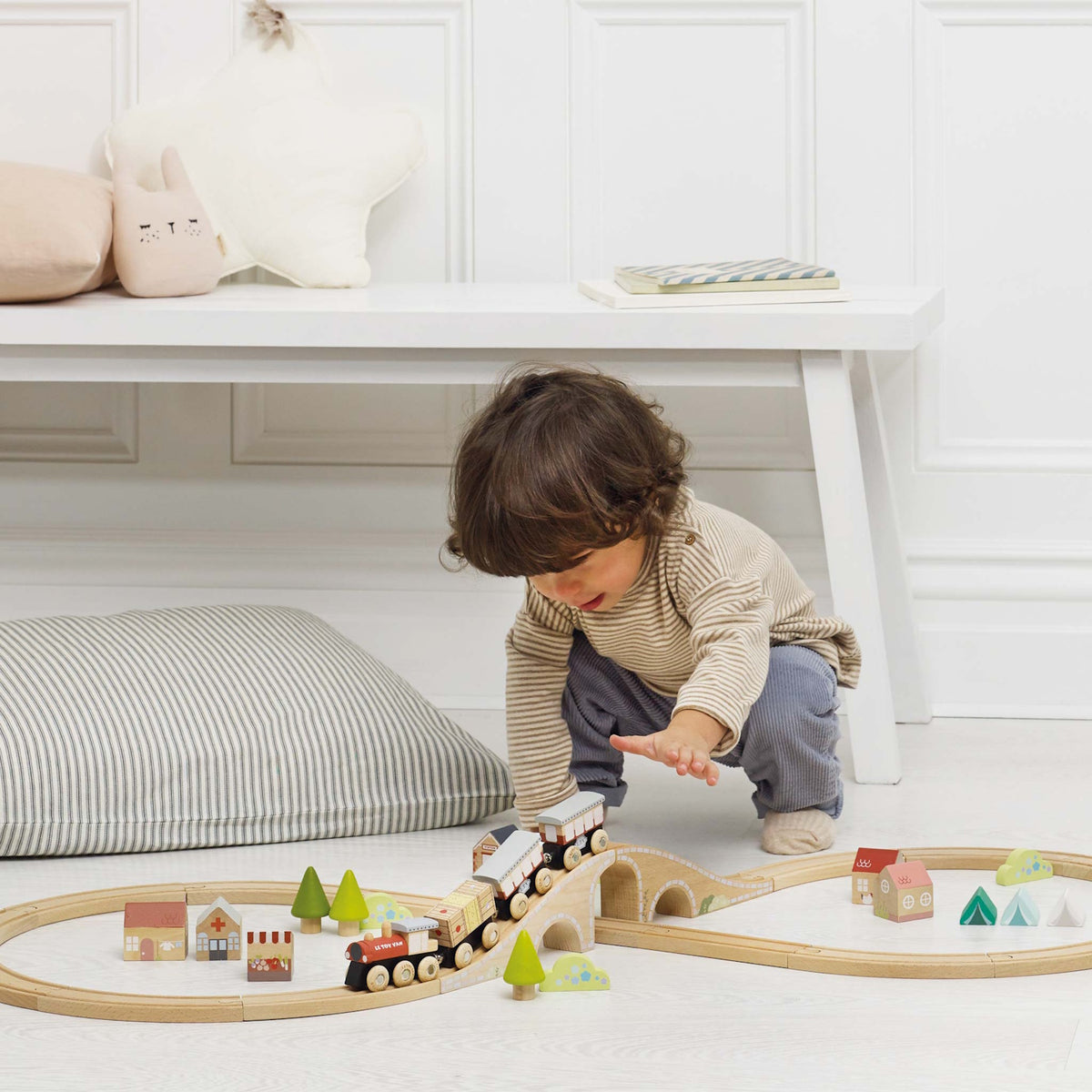 Toddler crouching down while playing with a wooden train set on a figure-8 track on the floor.