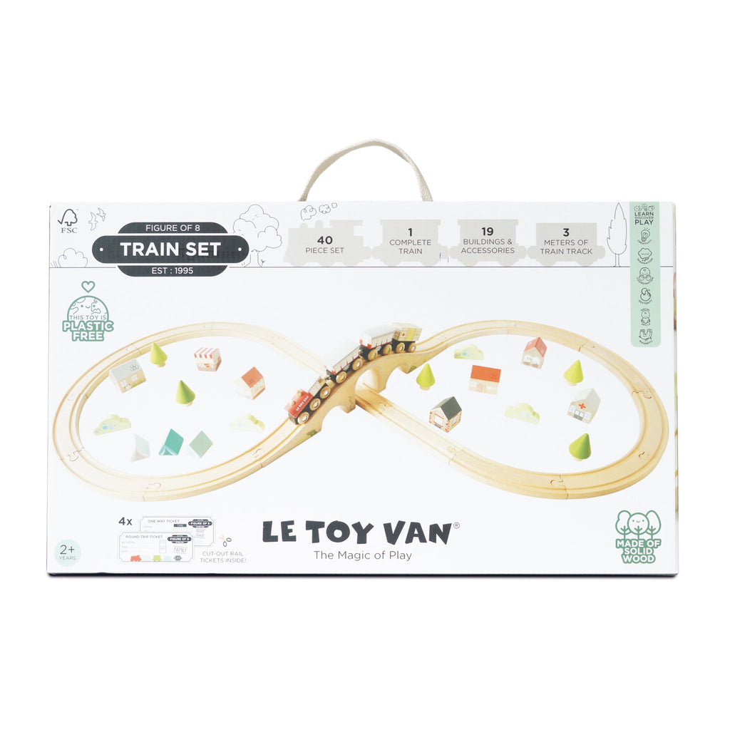 Box for "Le Toy Van" train set featuring a wooden figure-eight track, colorful trains, and accessories. Labels highlight it's plastic-free and made from solid wood.