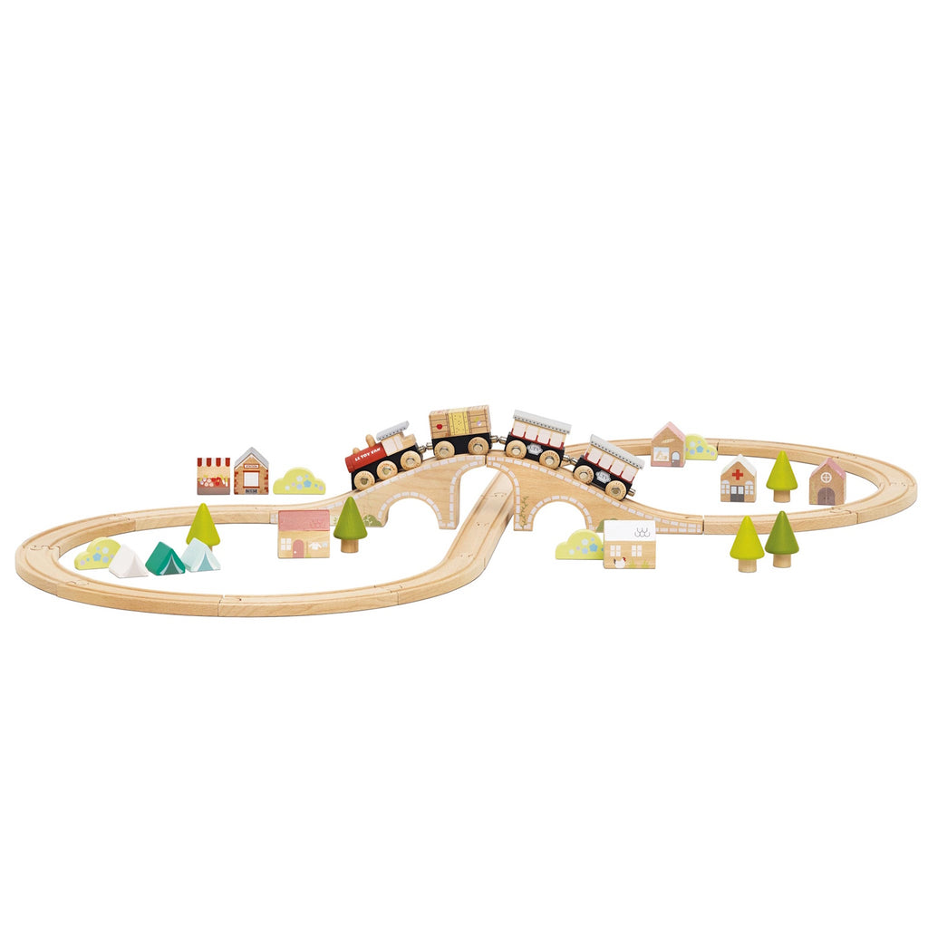 Wooden toy train set with a bridge and winding tracks is surrounded by small wooden trees and houses, creating a playful village scene.