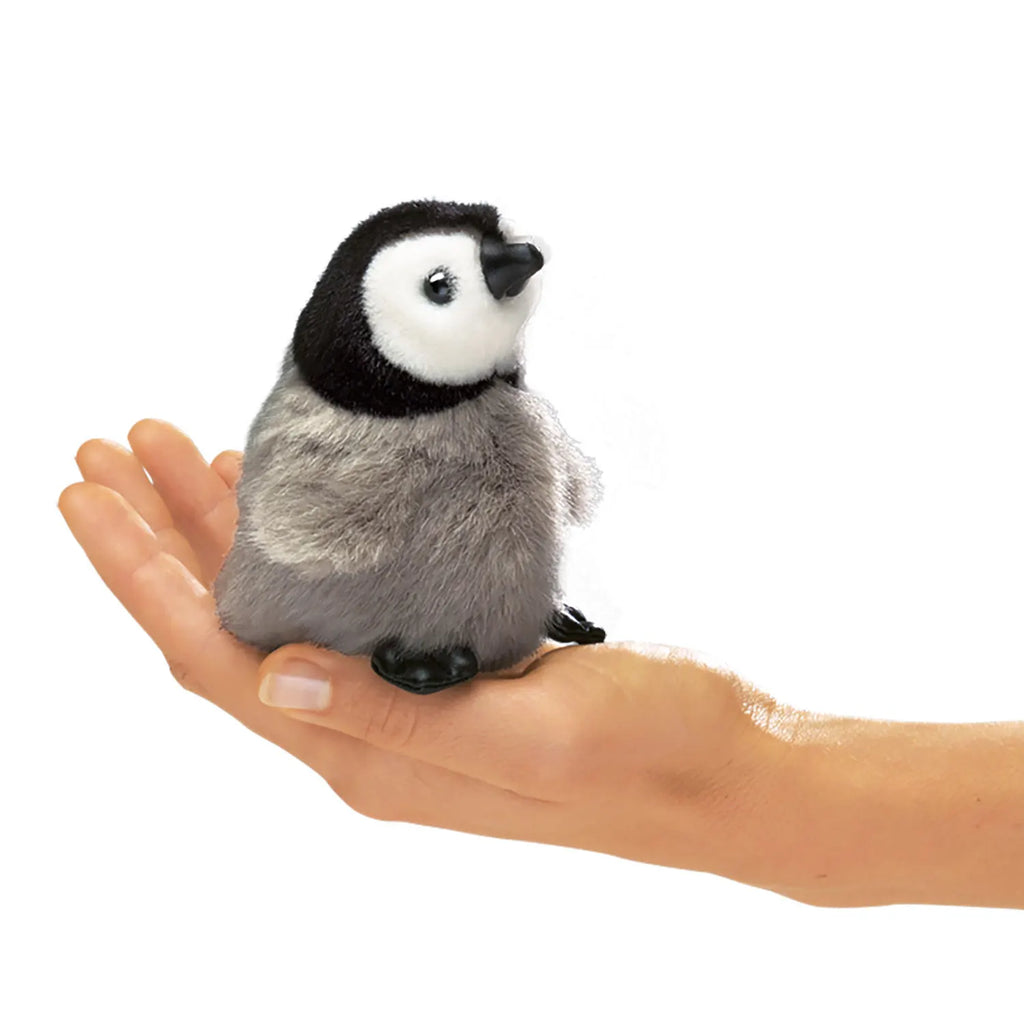 A small, fluffy toy penguin chick with black and white markings sits on a human palm, evoking a sense of cuteness and gentle care.