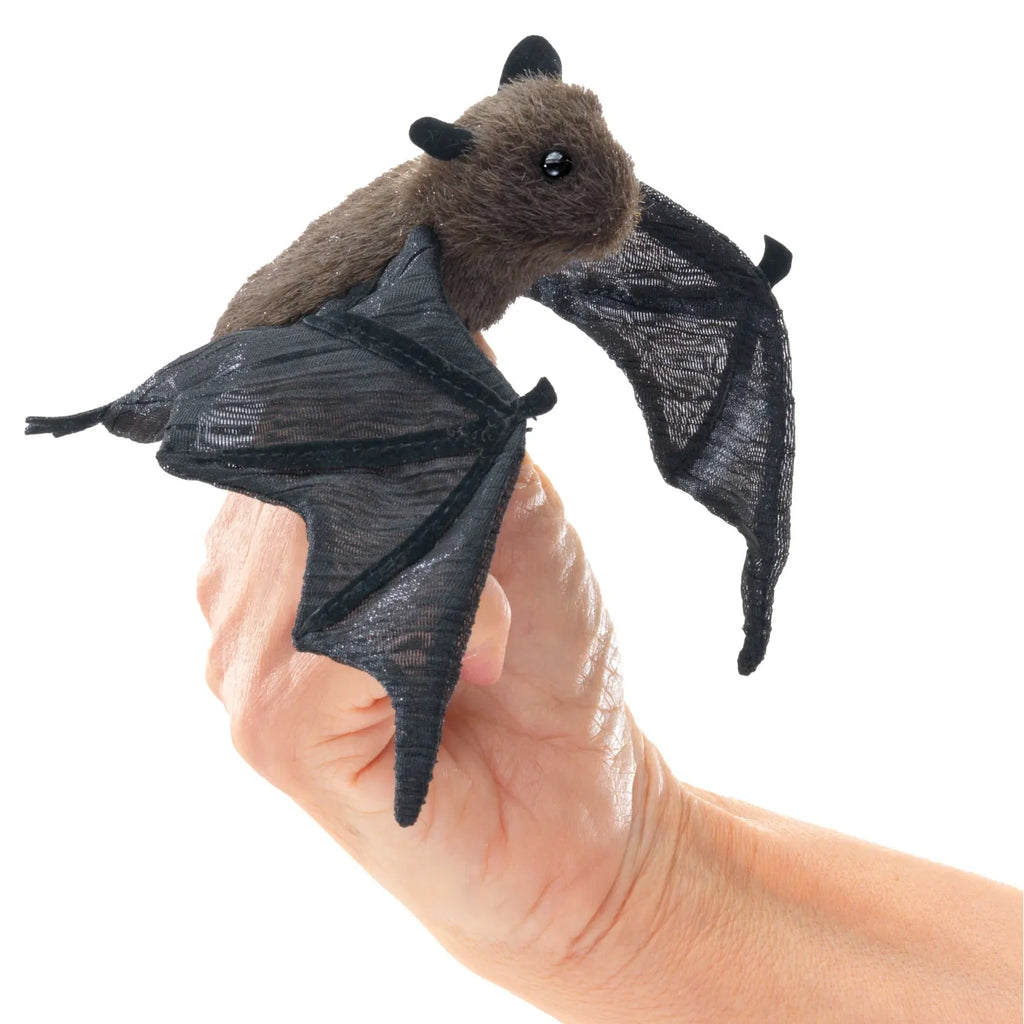 A tiny plush bat puppet with dark wings and a soft brown body sits on a person's fingers. The bat's wide eyes and small ears give it a cute appearance.
