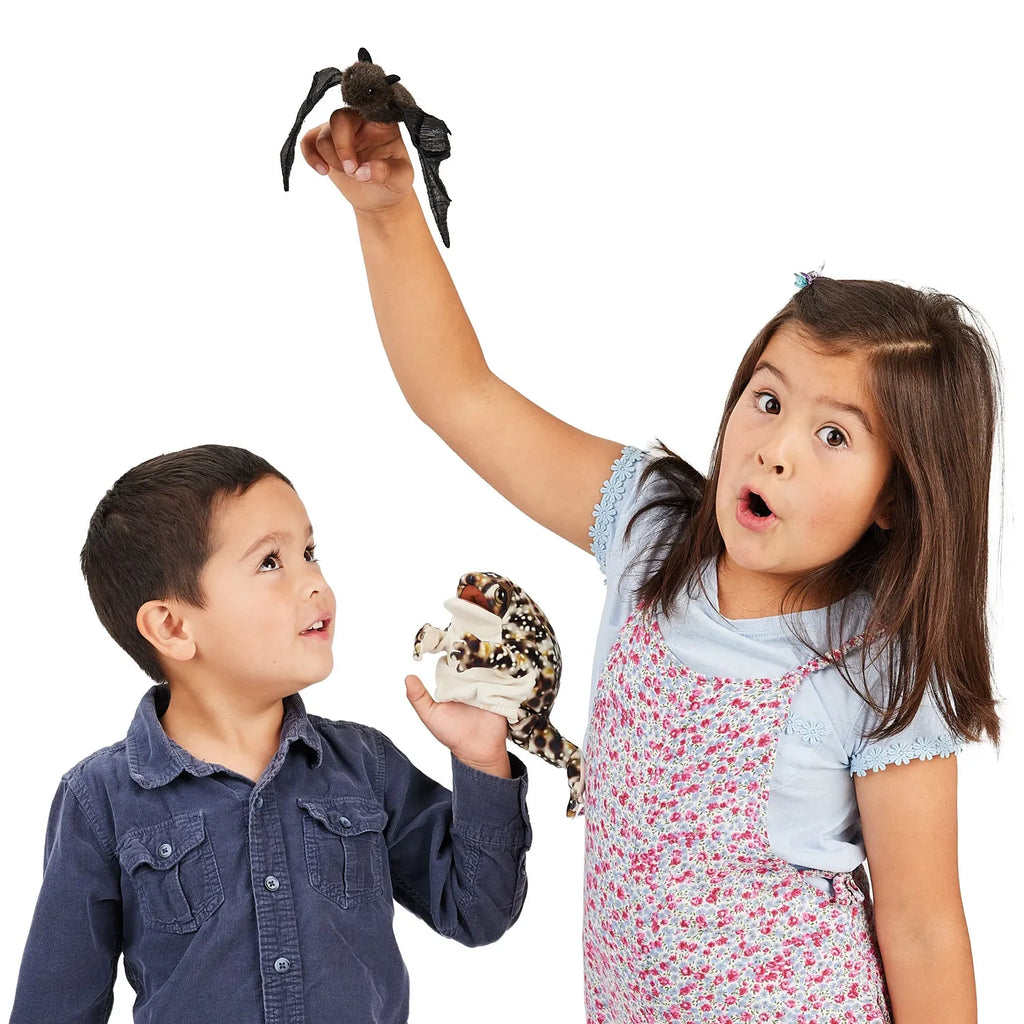 Two children look amazed. The girl holds a toy bat high, with a surprised expression. The boy, wearing a blue shirt, looks up smiling, holding a shark model.