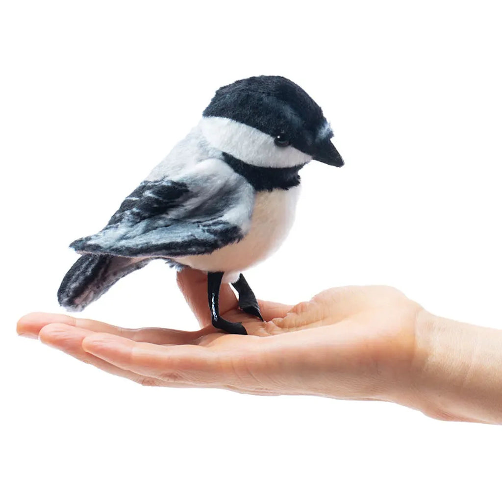 A plush chickadee toy sits on an open hand against a white background. The toy's soft, realistic features evoke a sense of calm and gentleness.