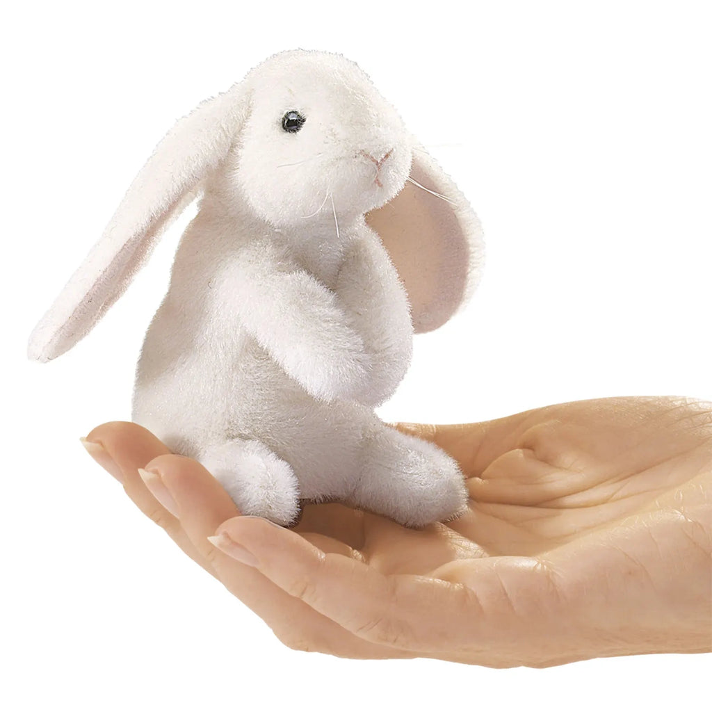 A tiny, white plush rabbit with long ears sits in an open palm, against a white background. The scene feels gentle and whimsical.